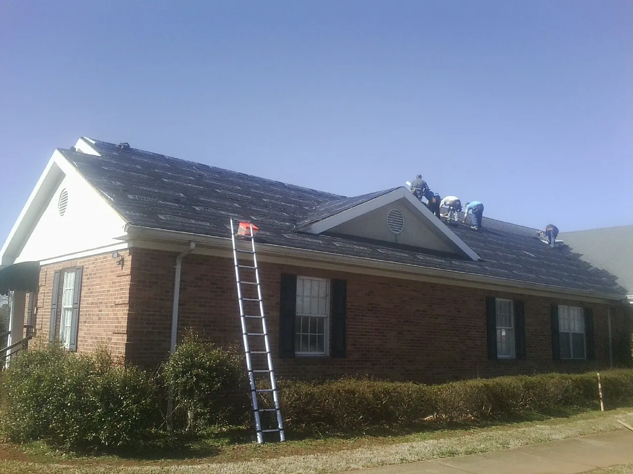 Crew tearing shingles off a brick ranch roof with a ladder set — Metal Roof Repair work by our crew in Kimberly